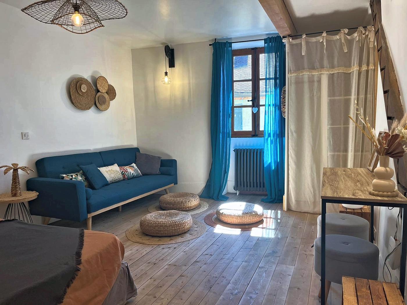 The sitting room in La Mercantine: blue sofa, shuttered window and woven poufs