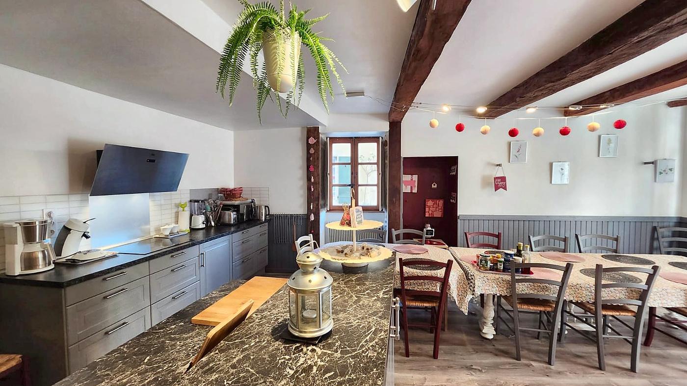 The kitchen seen from the island, the big table under the beams and its string lights