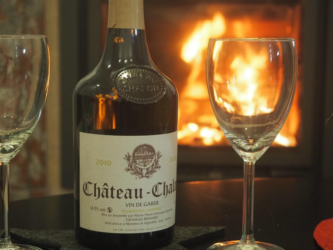 A bottle of Château-Chalon and two glasses set before the lit fireplace in the sitting room